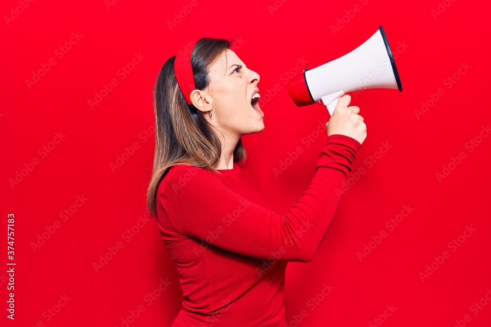 Young beautiful woman wearing diadem with angry expression. Screaming loud using megaphone standing over isolated red background Young beautiful woman wearing diadem with angry expression. Screaming loud using megaphone standing over isolated red background