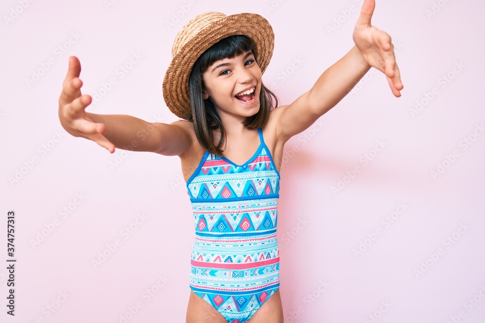 Young little girl with bang wearing swimsuit and summer hat looking at
