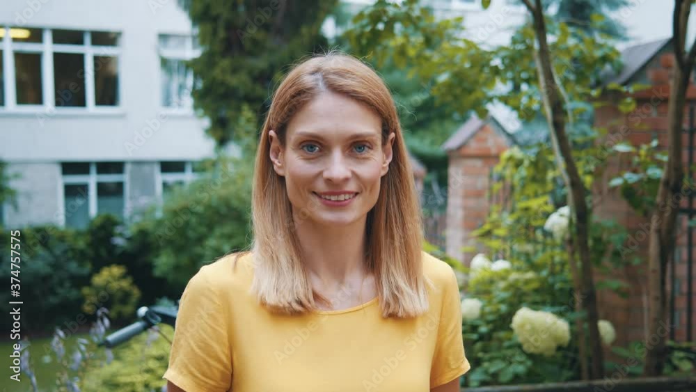 Portrait of attractive middle aged woman with cheerful smile looking confident and healhy standing in beautiful green coutyard outside. Portrait of attractive middle aged woman with cheerful smile looking confident and healhy standing in beautiful green coutyard outside.