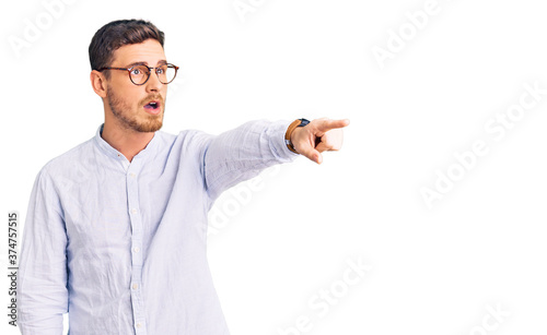 Handsome young man with bear wearing elegant business shirt and glasses pointing with finger surprised ahead, open mouth amazed expression, something on the front