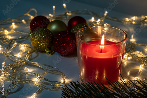 Red christmas candle, burning candle fire on a table with holiday garland and pine tree decorations and balls