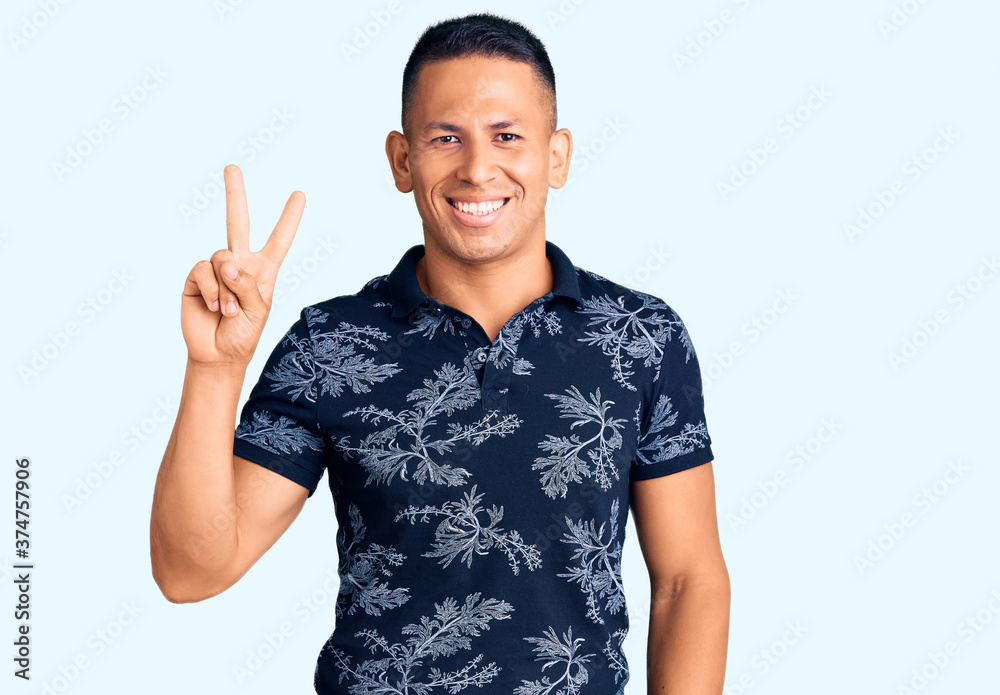 Young handsome latin man wearing casual clothes smiling with happy face winking at the camera doing victory sign. number two. Young handsome latin man wearing casual clothes smiling with happy face winking at the camera doing victory sign. number two.