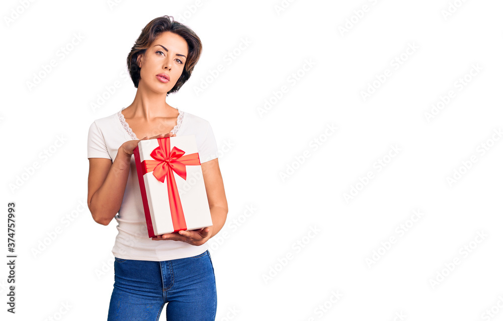 Fototapeta premium Young beautiful woman holding gift thinking attitude and sober expression looking self confident
