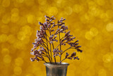 Dry flowers in metal vase on blurred yellow background