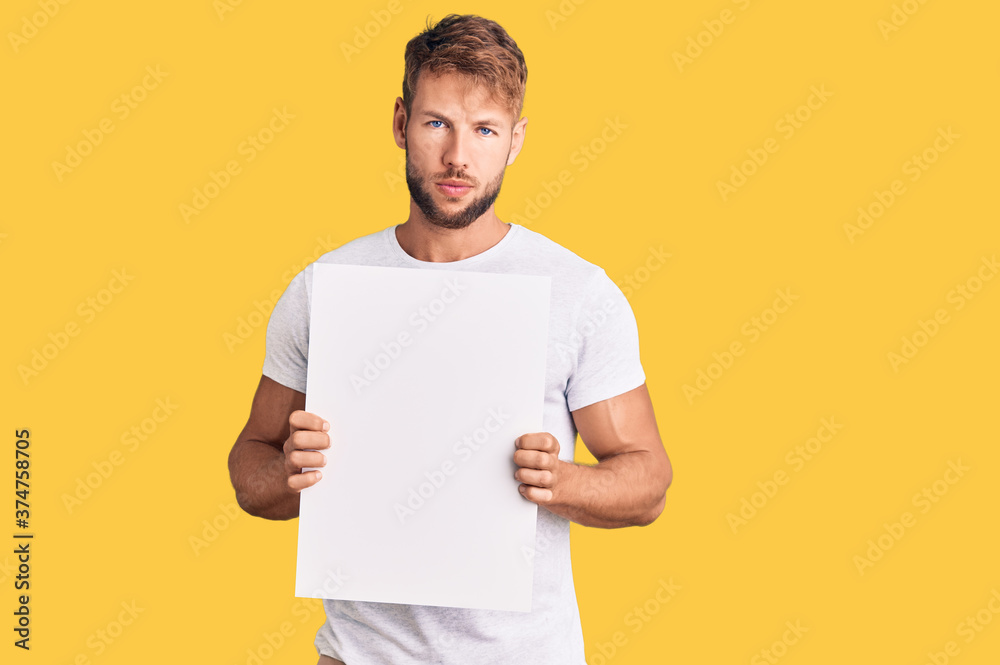 Young caucasian man holding blank empty banner thinking attitude and sober expression looking self confident Young caucasian man holding blank empty banner thinking attitude and sober expression looking self confident
