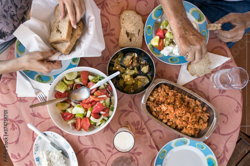 Top view of a Greek lunch meal at summer with omellete, horiatiki salad, feta cheese, grilled vegetables and bread.