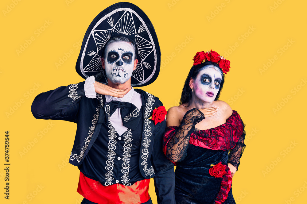 Fototapeta premium Young couple wearing mexican day of the dead costume over background cutting throat with hand as knife, threaten aggression with furious violence