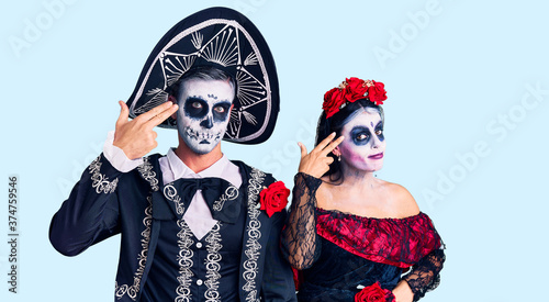 Young couple wearing mexican day of the dead costume over background shooting and killing oneself pointing hand and fingers to head like gun, suicide gesture.
