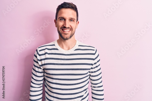 Young handsome man wearing casual striped sweater standing over isolated pink background with a happy and cool smile on face. Lucky person.