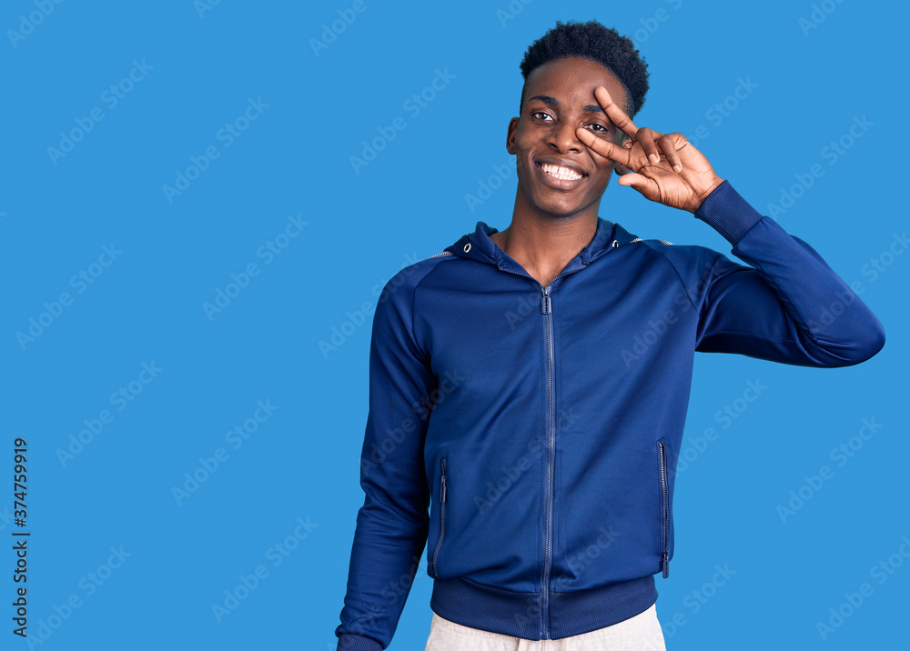 Young african american man wearing sportswear doing peace symbol with fingers over face, smiling cheerful showing victory Young african american man wearing sportswear doing peace symbol with fingers over face, smiling cheerful showing victory