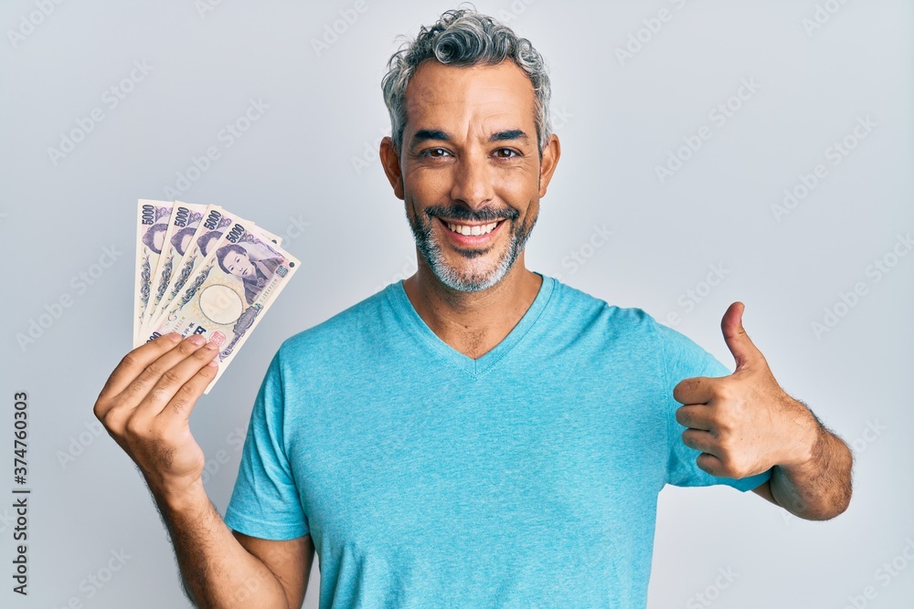 Middle age grey-haired man holding japanese yen banknotes smiling happy and positive, thumb up doing excellent and approval sign Middle age grey-haired man holding japanese yen banknotes smiling happy and positive, thumb up doing excellent and approval sign