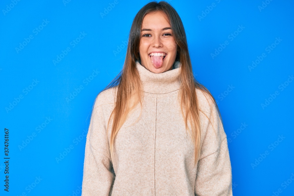 Fototapeta premium Beautiful caucasian woman wearing wool winter sweater sticking tongue out happy with funny expression. emotion concept.