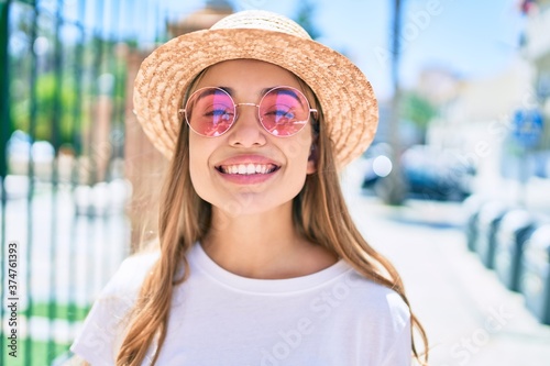 Young beautiful blonde caucasian woman smiling happy outdoors on a sunny day wearing summer hat and pink sunglasses
