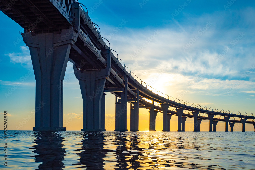 Fototapeta premium Road bridge at sunset. Two-level bridge over the water. Highway over the Bay. The highway passes over the river. A long bridge over the water and the setting sun.