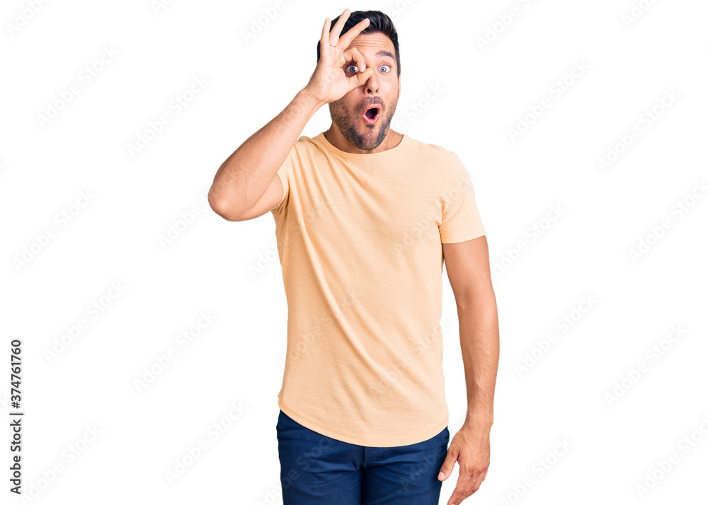 Fototapeta premium Young hispanic man wearing casual clothes doing ok gesture shocked with surprised face, eye looking through fingers. unbelieving expression.