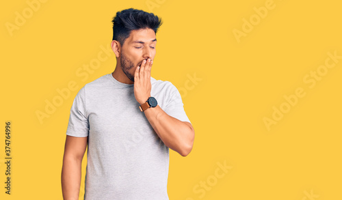 Handsome latin american young man wearing casual tshirt bored yawning tired covering mouth with hand. restless and sleepiness.