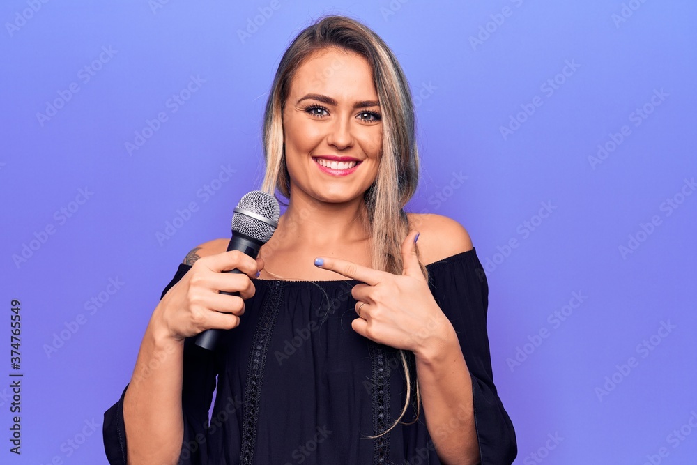 Young beautiful blonde singer woman singing using microphone over purple background smiling happy pointing with hand and finger Young beautiful blonde singer woman singing using microphone over purple background smiling happy pointing with hand and finger