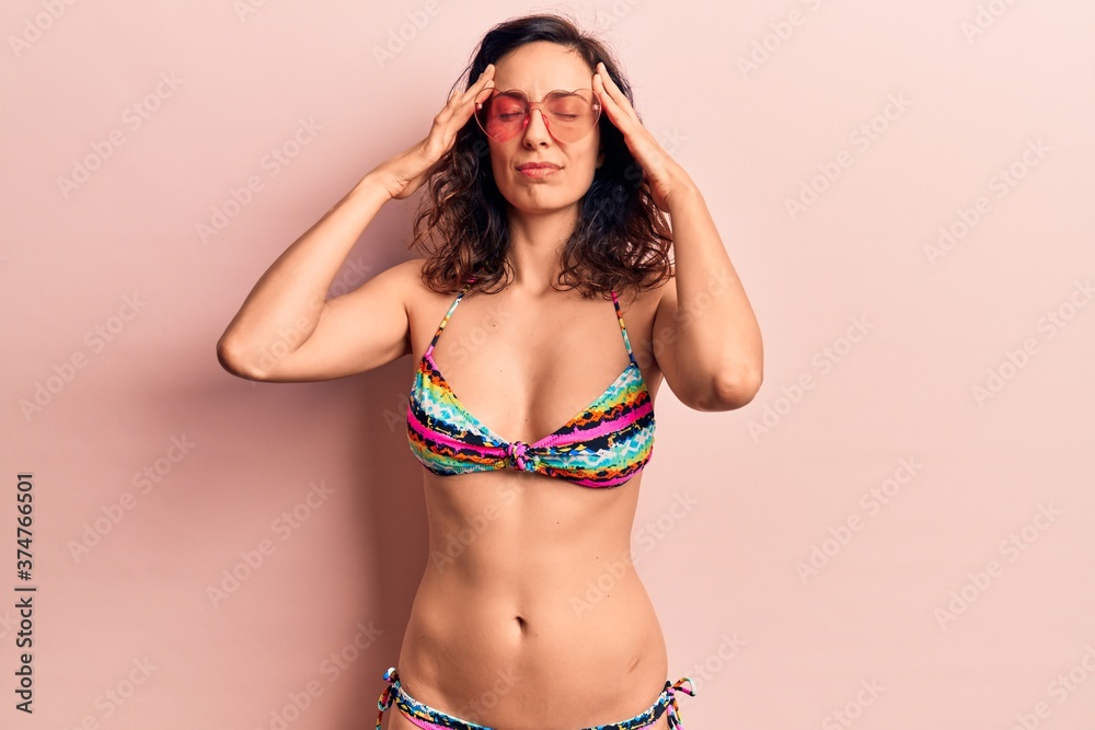 Obraz premium Young beautiful hispanic woman wearing bikini and heart sunglasses with hand on head, headache because stress. suffering migraine.