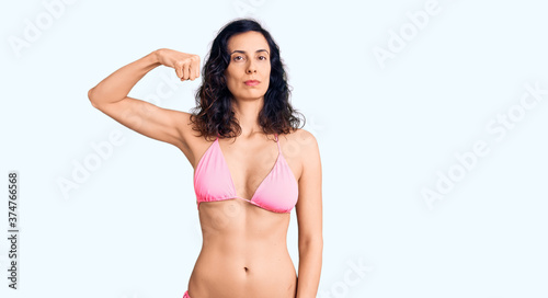 Young beautiful hispanic woman wearing bikini strong person showing arm muscle, confident and proud of power © Krakenimages.com