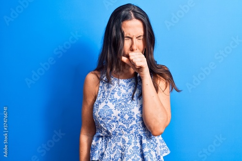 Young beautiful brunette woman wearing casual sleeveless t-shirt over blue background feeling unwell and coughing as symptom for cold or bronchitis. Health care concept.