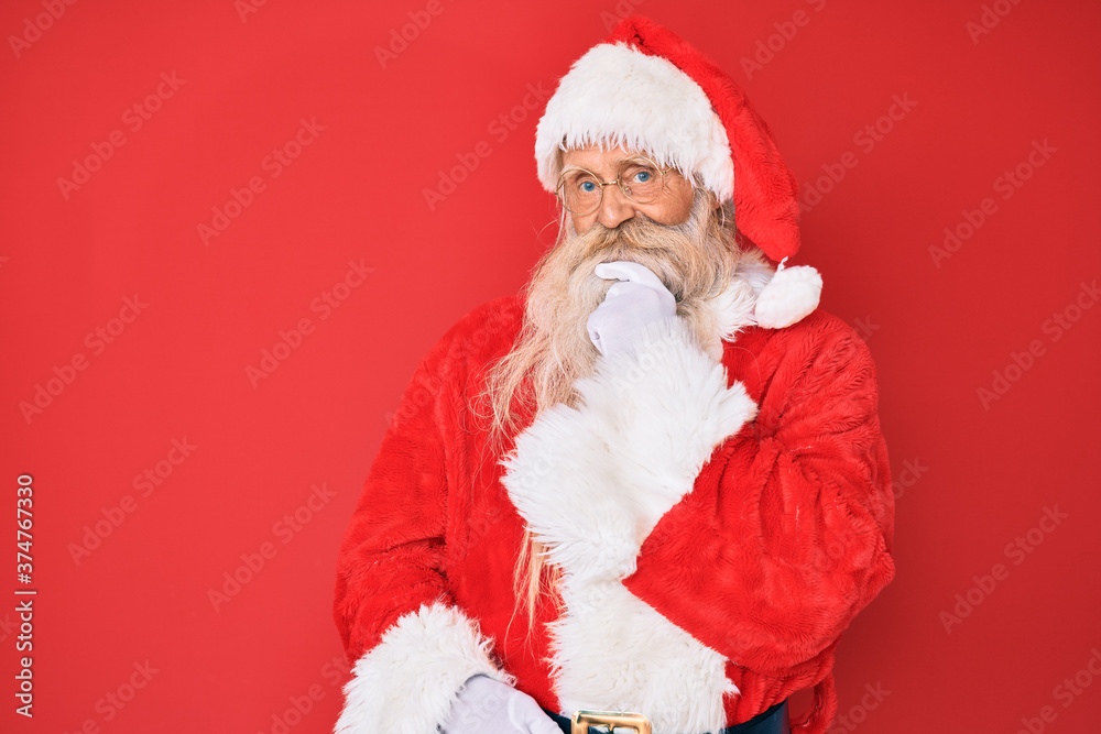 Old senior man with grey hair and long beard wearing traditional santa claus costume looking confident at the camera with smile with crossed arms and hand raised on chin. thinking positive. Old senior man with grey hair and long beard wearing traditional santa claus costume looking confident at the camera with smile with crossed arms and hand raised on chin. thinking positive.
