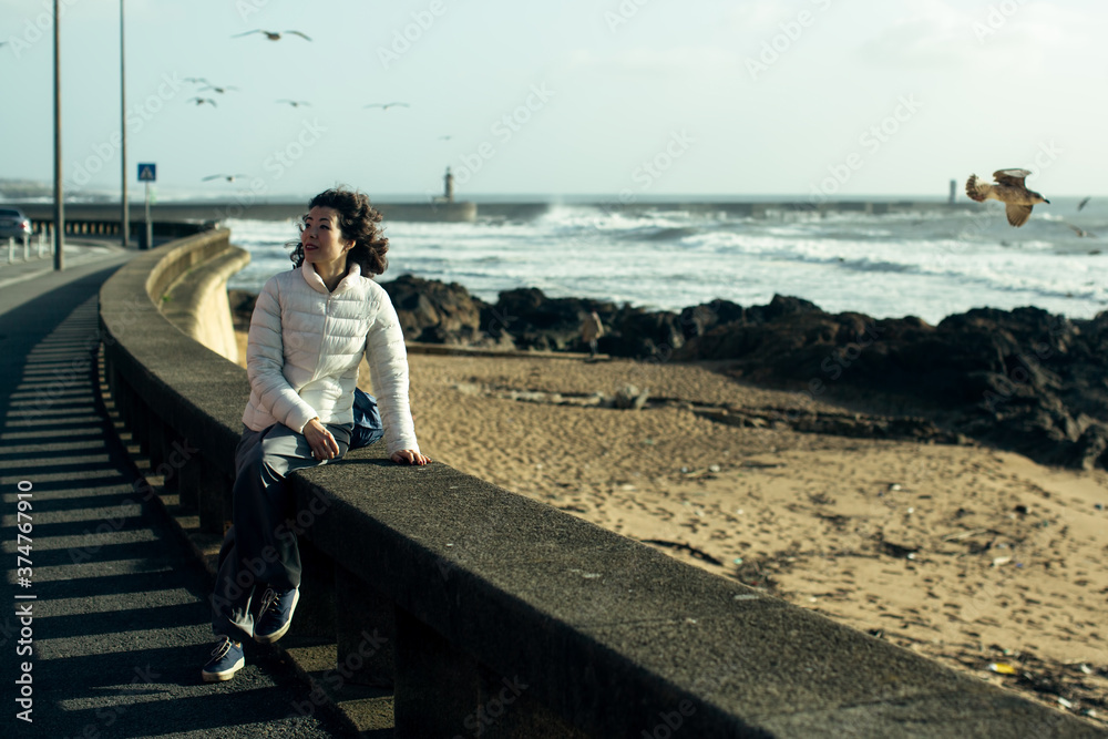 Asian woman sits on the waterfront during the surf and gulls around. Asian woman sits on the waterfront during the surf and gulls around.