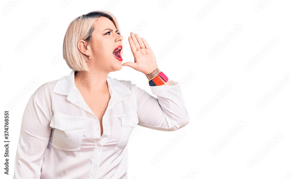 Young blonde plus size woman wearing casual shirt shouting and screaming loud to side with hand on mouth. communication concept. Young blonde plus size woman wearing casual shirt shouting and screaming loud to side with hand on mouth. communication concept.