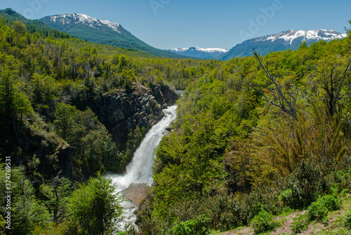 waterfall among pine forest with snowy mountains in the background