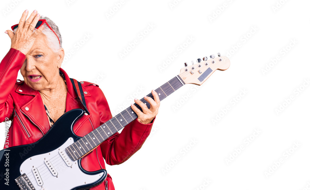 Senior beautiful woman with blue eyes and grey hair wearing a modern look playing electric guitar surprised with hand on head for mistake, remember error. forgot, bad memory concept.