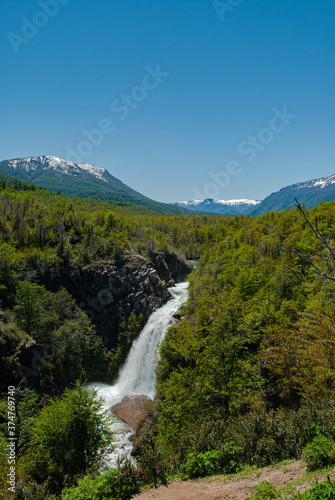 waterfall among pine forest with snowy mountains in the background