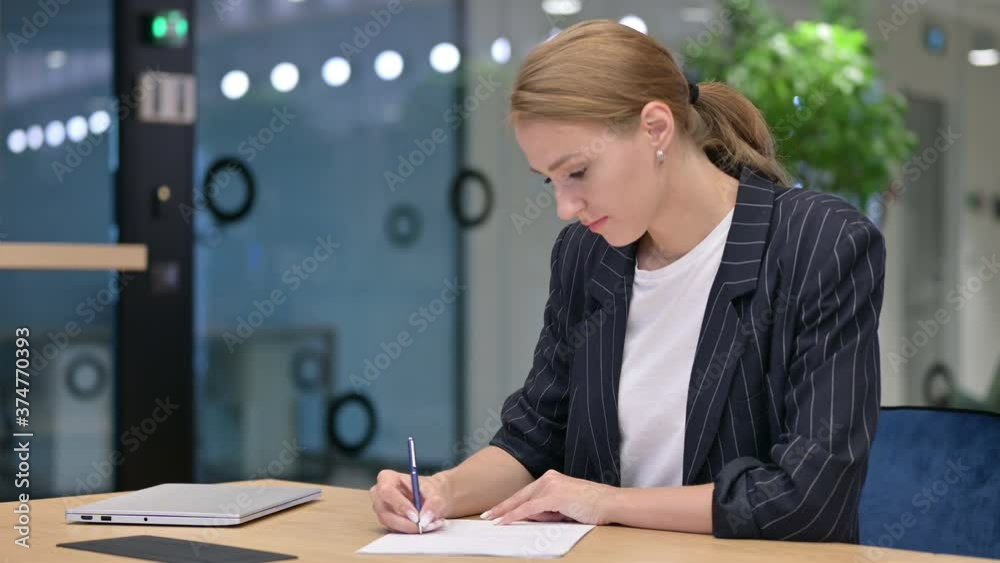 Serious Businesswoman Writing on Paper in Office Serious Businesswoman Writing on Paper in Office