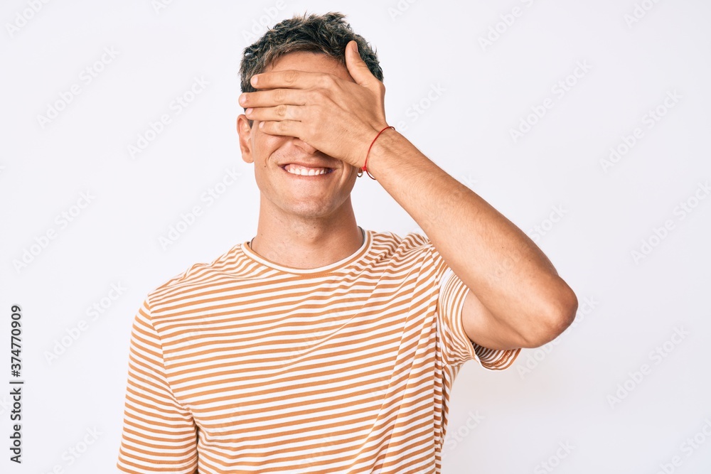 Young handsome man wearing casual clothes smiling and laughing with hand on face covering eyes for surprise. blind concept. Young handsome man wearing casual clothes smiling and laughing with hand on face covering eyes for surprise. blind concept.