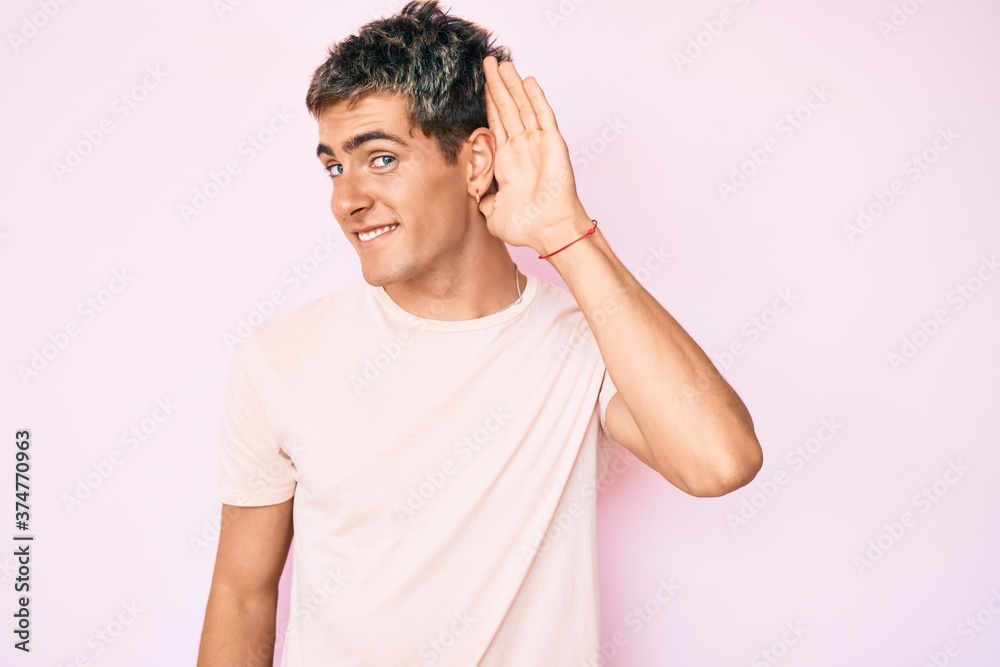 Young handsome man wearing casual clothes smiling with hand over ear listening and hearing to rumor or gossip. deafness concept. Young handsome man wearing casual clothes smiling with hand over ear listening and hearing to rumor or gossip. deafness concept.