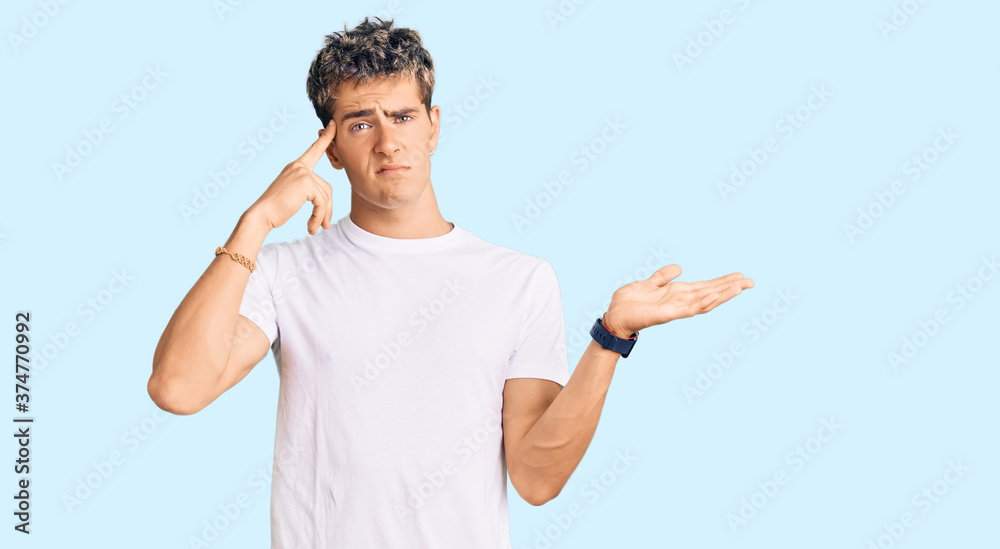 Young handsome man wearing casual white tshirt confused and annoyed with open palm showing copy space and pointing finger to forehead. think about it. Young handsome man wearing casual white tshirt confused and annoyed with open palm showing copy space and pointing finger to forehead. think about it.