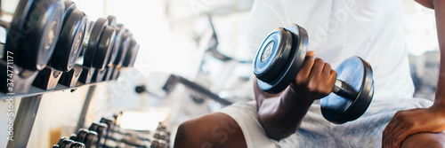 Obraz na plátně Young African American man sitting and lifting a dumbbell close to the rack at gym