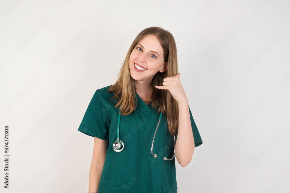 Female doctor wearing a green scrubs and stethoscope smiling doing phone gesture with hand and fingers like talking on the telephone. Communicating concepts. Female doctor wearing a green scrubs and stethoscope smiling doing phone gesture with hand and fingers like talking on the telephone. Communicating concepts.