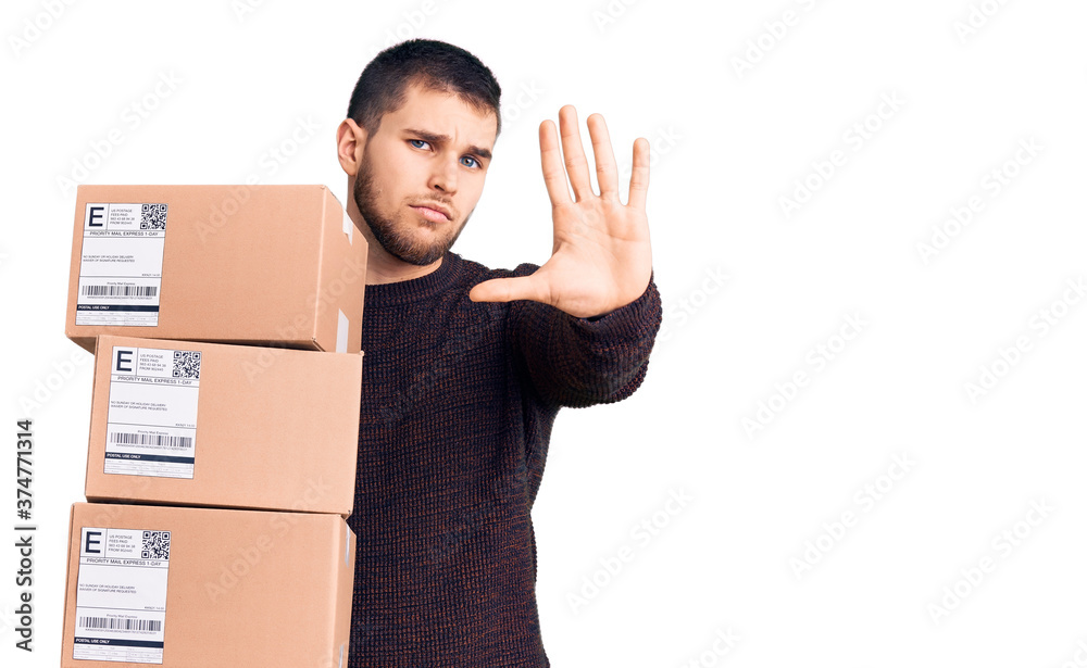 Young handsome man holding delivery package with open hand doing stop sign with serious and confident expression, defense gesture Young handsome man holding delivery package with open hand doing stop sign with serious and confident expression, defense gesture