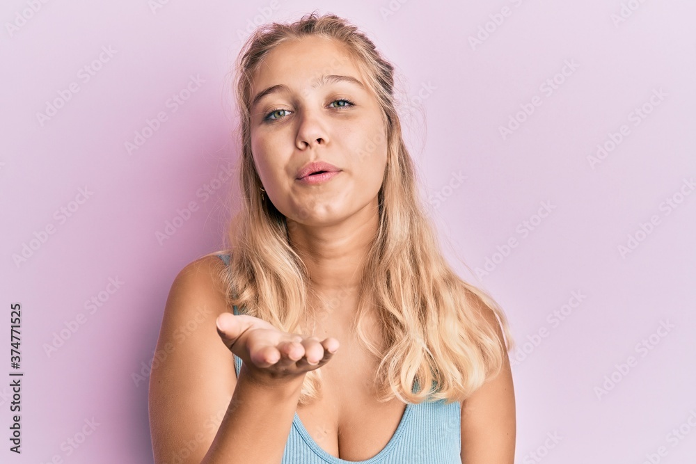 Young blonde girl wearing casual clothes looking at the camera blowing a kiss with hand on air being lovely and sexy. love expression. Young blonde girl wearing casual clothes looking at the camera blowing a kiss with hand on air being lovely and sexy. love expression.