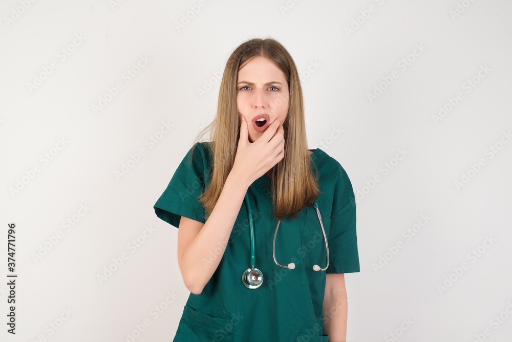 Female doctor wearing a green scrubs and stethoscope Looking fascinated with disbelief, surprise and amazed expression with hands on chin Female doctor wearing a green scrubs and stethoscope Looking fascinated with disbelief, surprise and amazed expression with hands on chin
