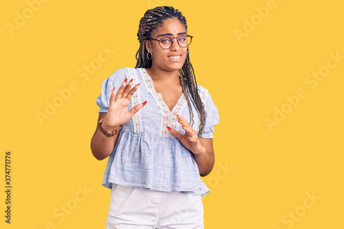 Young african american woman with braids wearing casual summer clothes and glasses disgusted expression, displeased and fearful doing disgust face because aversion reaction. with hands raised