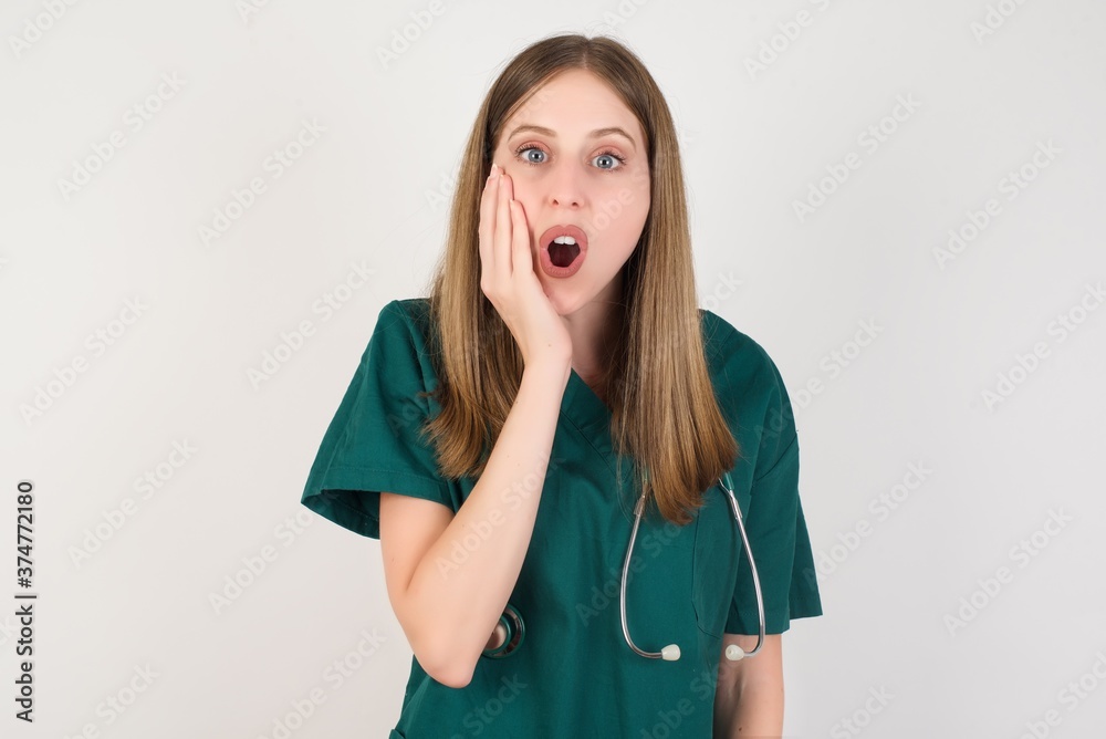 Horizontal portrait of shocked Female doctor wearing a green scrubs and stethoscope looks with great surprisment being very stunned, astonished with unexpected news, . Facial expressions concept. Horizontal portrait of shocked Female doctor wearing a green scrubs and stethoscope looks with great surprisment being very stunned, astonished with unexpected news, . Facial expressions concept.