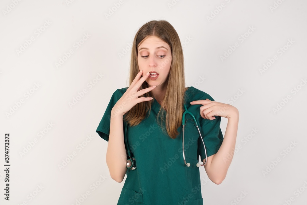 Shocked Female doctor wearing a green scrubs and stethoscope look surprisedly down, indicates at blank with fore finger, . Scared male finds out price on usual shirt from luxury shop Shocked Female doctor wearing a green scrubs and stethoscope look surprisedly down, indicates at blank with fore finger, . Scared male finds out price on usual shirt from luxury shop