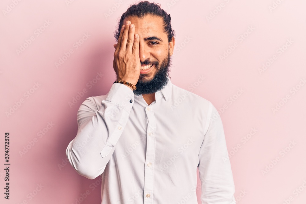 Young arab man wearing casual clothes covering one eye with hand, confident smile on face and surprise emotion. Young arab man wearing casual clothes covering one eye with hand, confident smile on face and surprise emotion.