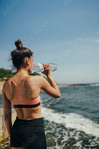 Woman drinking fresh water from bottle after exercise on beach