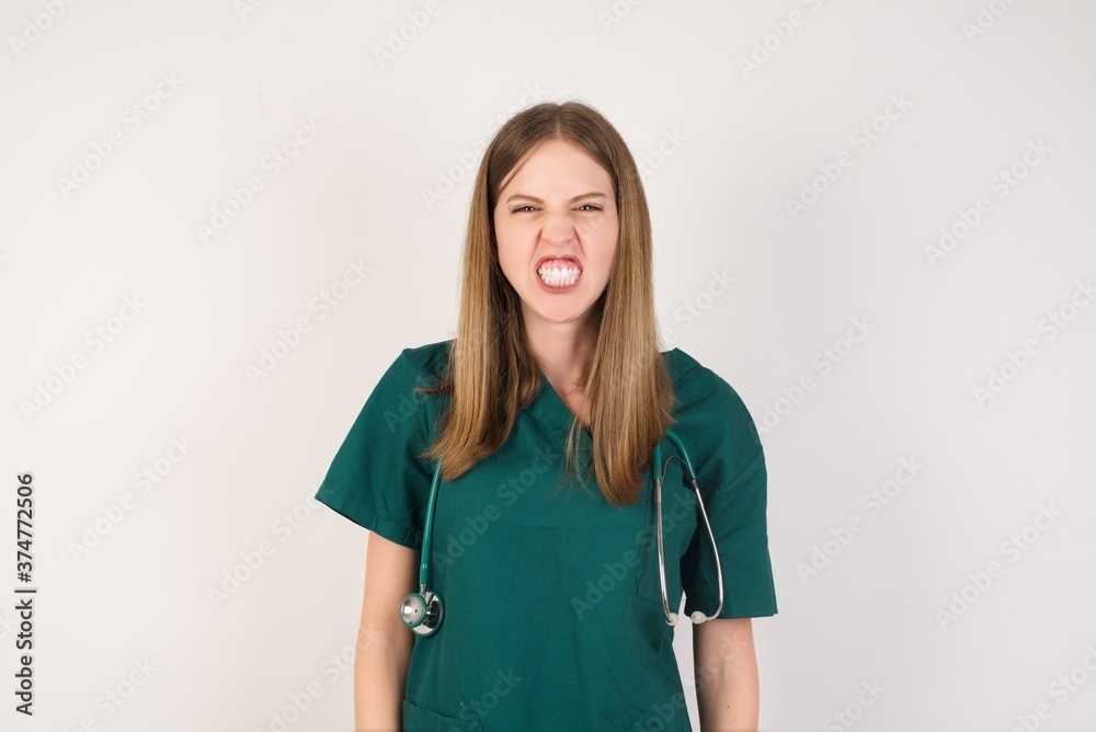 Portrait of angry Female doctor wearing a green scrubs , keeps teeth clenched, frowns face in dissatisfaction, irritated because of much duties. Furious man looks out of window, sees miserable weather Portrait of angry Female doctor wearing a green scrubs , keeps teeth clenched, frowns face in dissatisfaction, irritated because of much duties. Furious man looks out of window, sees miserable weather