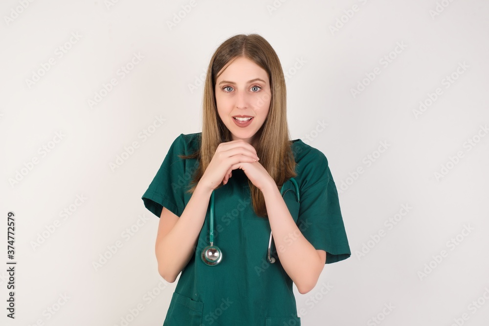 Female doctor wearing a green scrubs and stethoscope praying for luck has hands crossed near face, amazed and opening mouth looking front. Female doctor wearing a green scrubs and stethoscope praying for luck has hands crossed near face, amazed and opening mouth looking front.