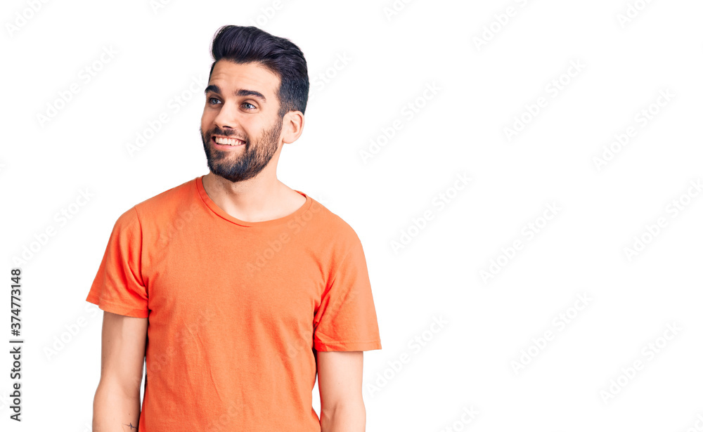 Young handsome man with beard wearing casual t-shirt looking away to side with smile on face, natural expression. laughing confident.