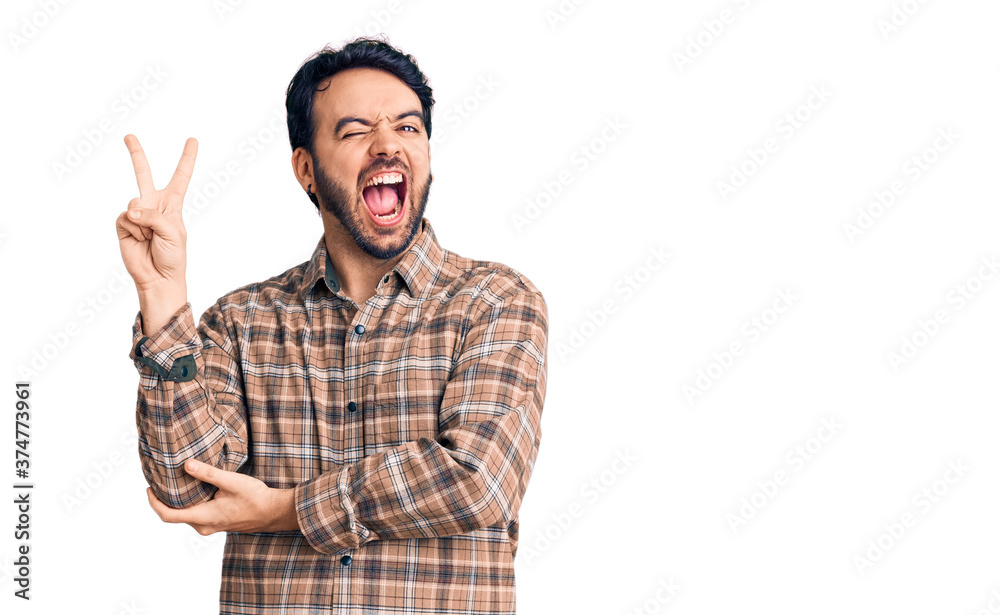 Young hispanic man wearing casual clothes smiling with happy face winking at the camera doing victory sign with fingers. number two. Young hispanic man wearing casual clothes smiling with happy face winking at the camera doing victory sign with fingers. number two.