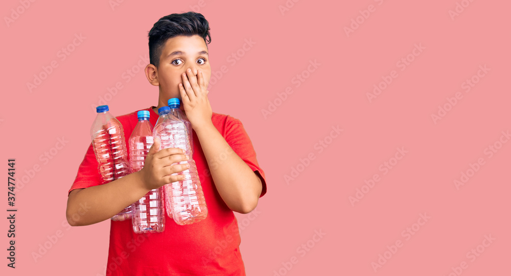 Little boy kid holding recycling plastic bottles covering mouth with hand, shocked and afraid for mistake. surprised expression Little boy kid holding recycling plastic bottles covering mouth with hand, shocked and afraid for mistake. surprised expression
