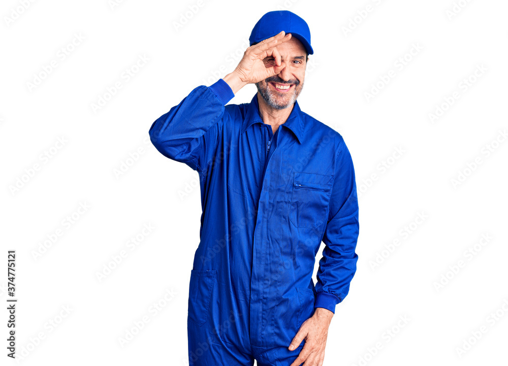 Middle age handsome man wearing mechanic uniform doing ok gesture with hand smiling, eye looking through fingers with happy face. Middle age handsome man wearing mechanic uniform doing ok gesture with hand smiling, eye looking through fingers with happy face.